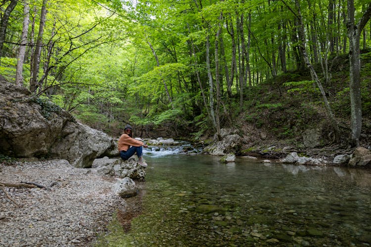 A Woman Sitting On The Rocky River