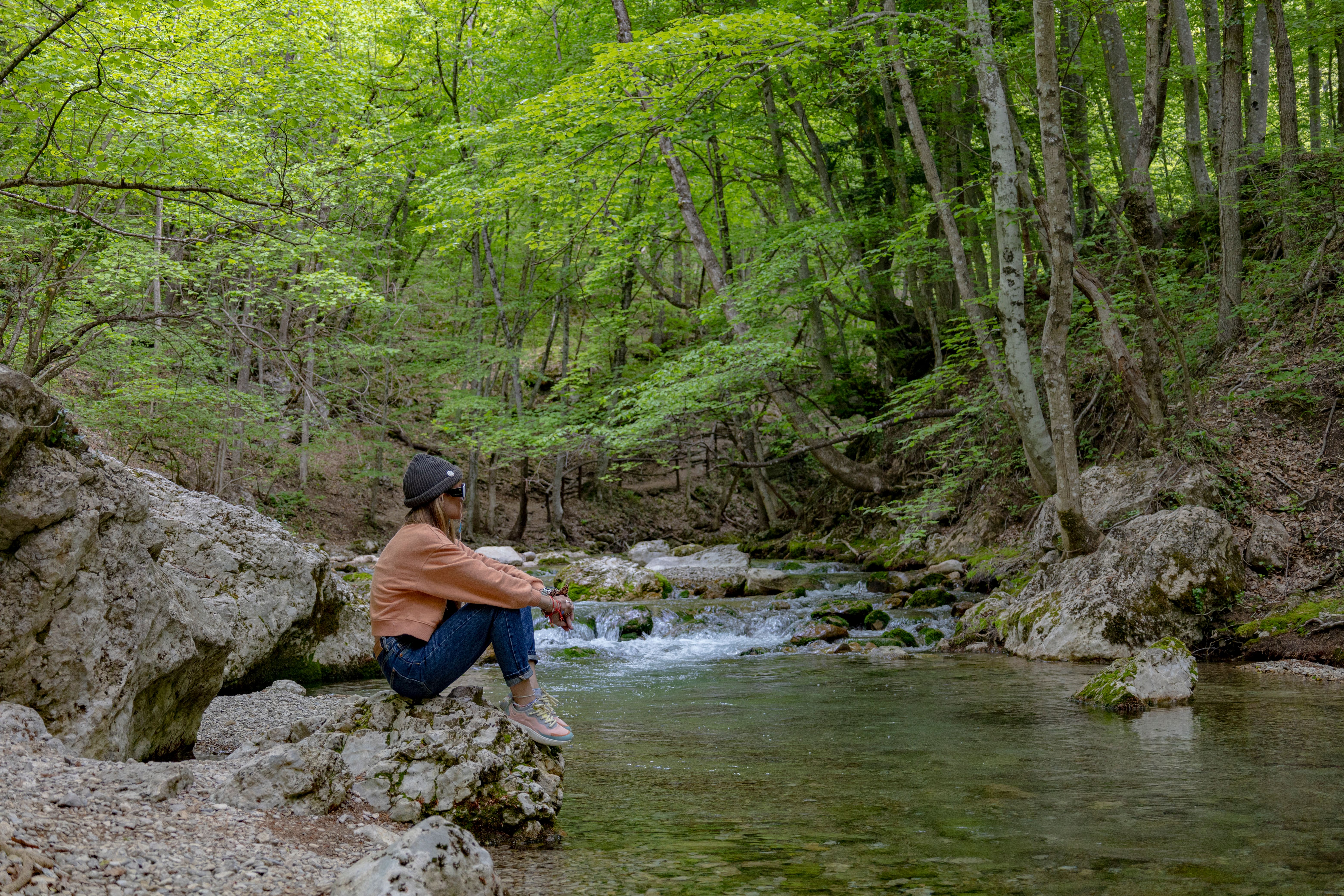 A woman sits by a peaceful forest stream, enjoying nature\'s tranquility.