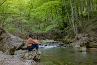 A Woman Sitting on a Rock by a River in a Forest