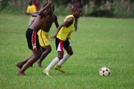 Action shot of teenage boys playing soccer outdoors on a grassy field in Kakamega, Kenya.