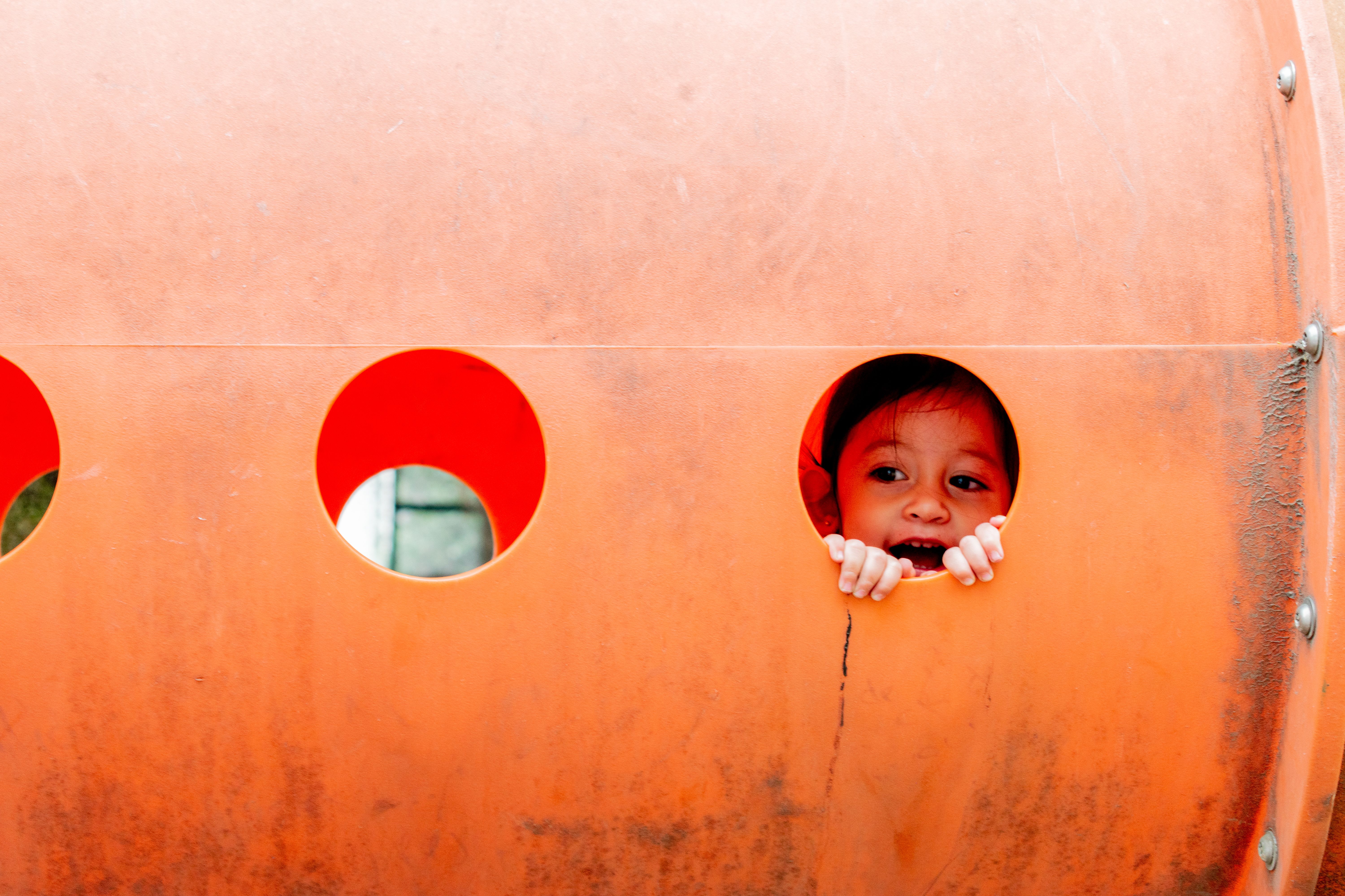 A joyful child peeks through a playground tunnel in Mexico City, capturing the essence of playful childhood.