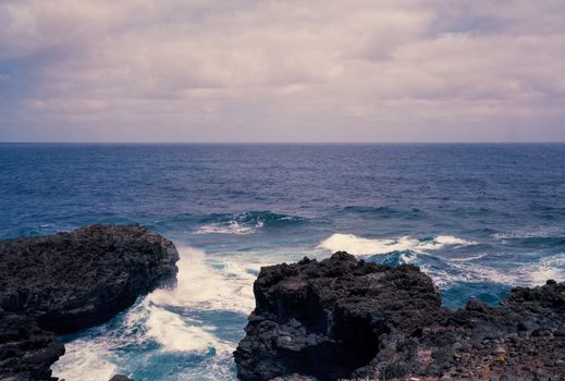 A stunning view of waves crashing against a rocky coastal landscape under a cloudy sky.