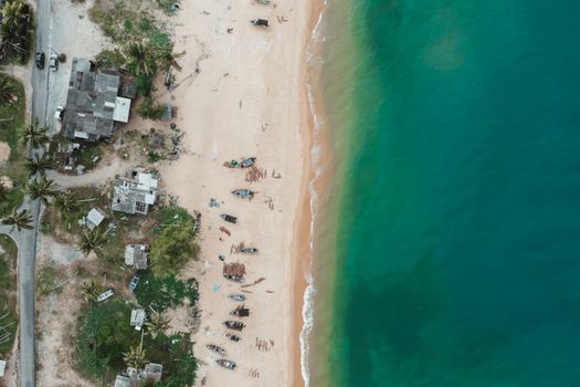 Stunning aerial shot of a tranquil beach with turquoise waters and rustic buildings.