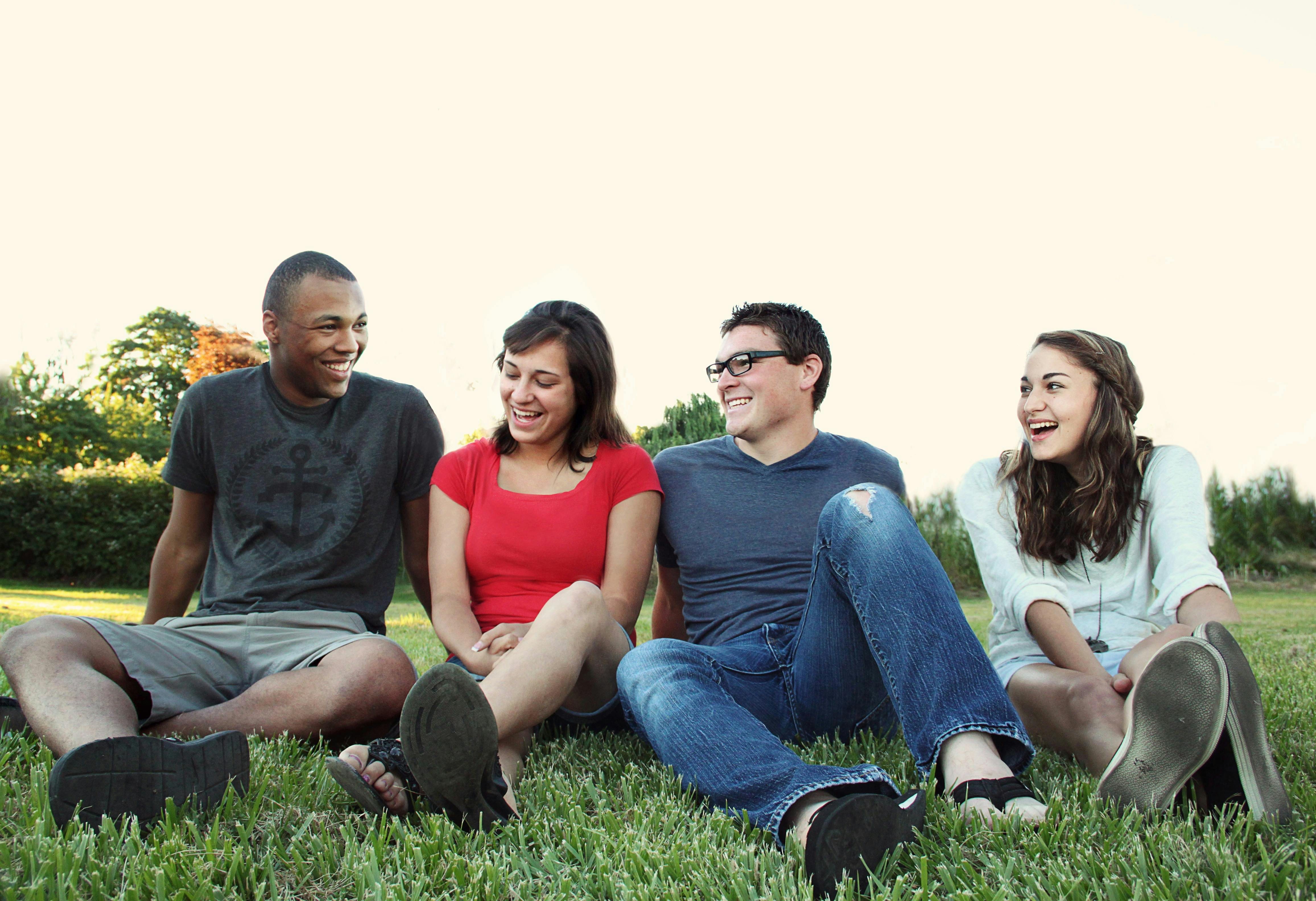 smiling women and men sitting on green grass