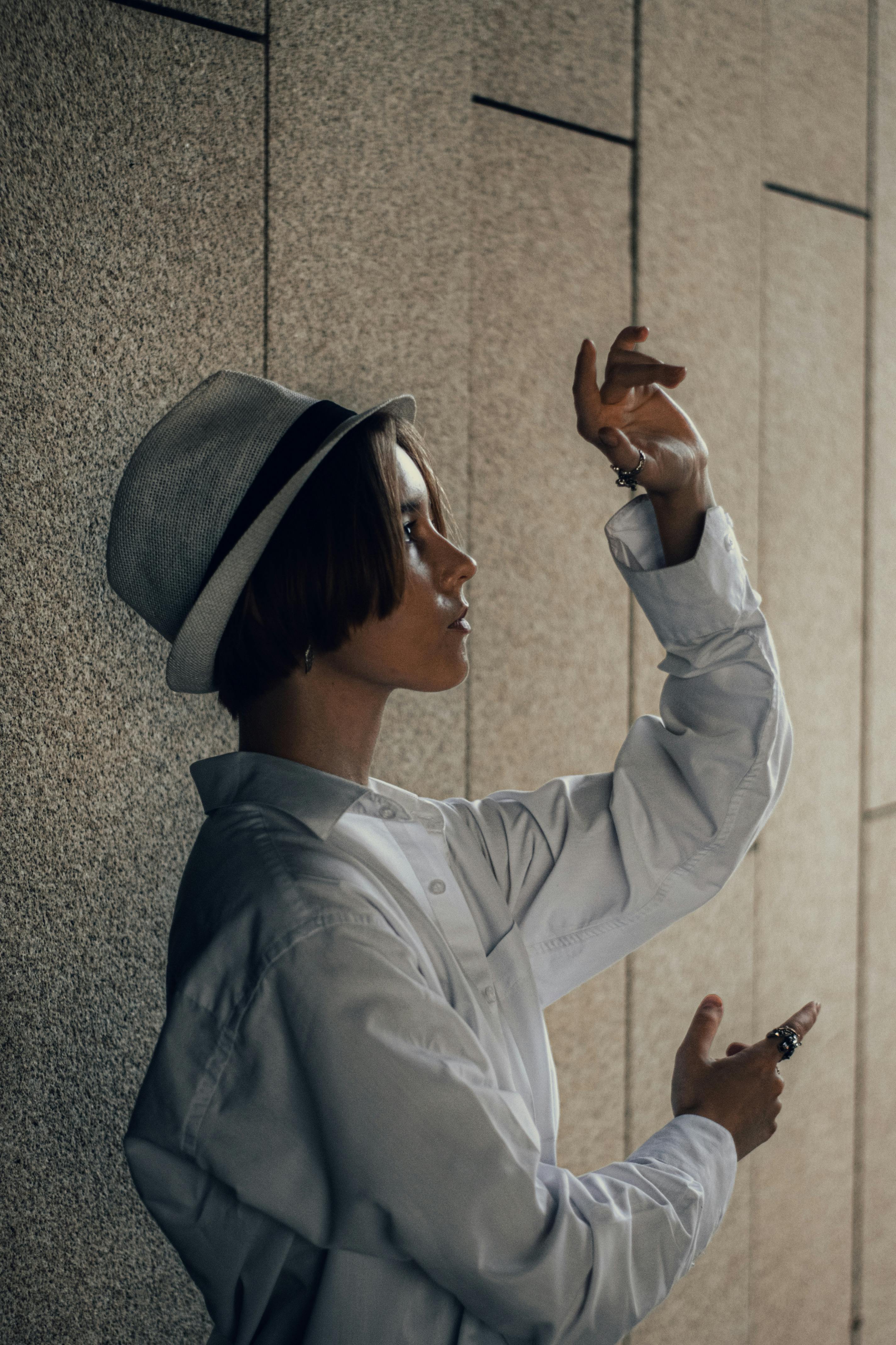 Profile of woman raising arms with artistic expression, wearing a hat and shirt.