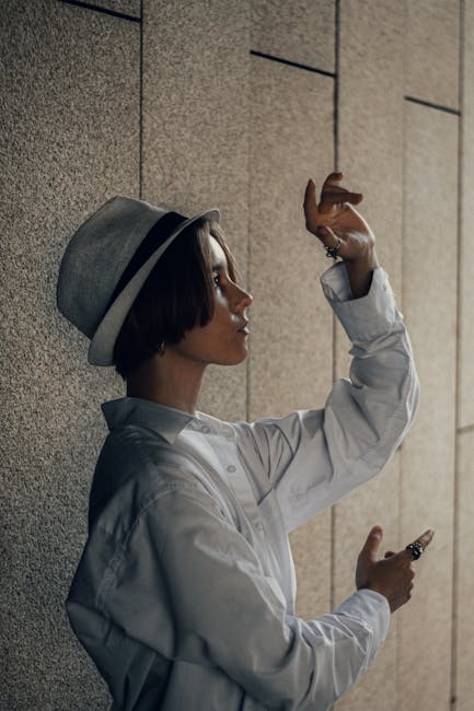 Profile of woman raising arms with artistic expression, wearing a hat and shirt.