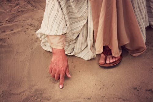 Человек, касающийся песка указательным пальцем правой руки