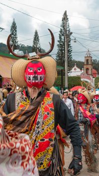 Colorful festival parade with masked performers in Calnali, Mexico, showcasing vibrant costumes.