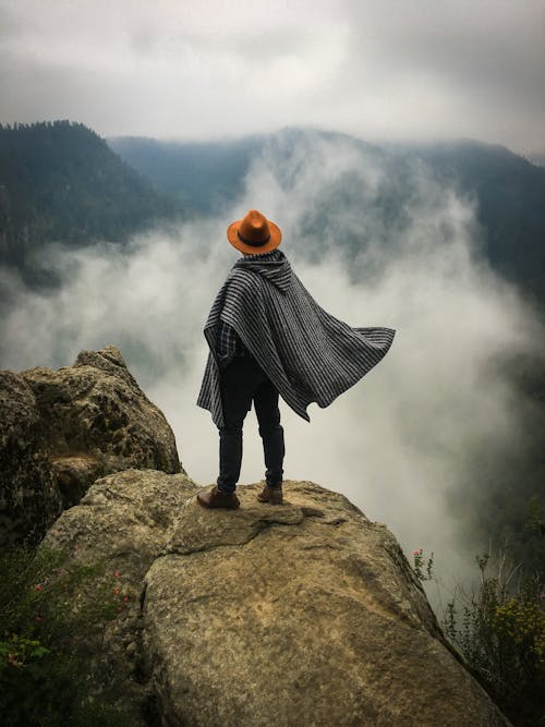 Free Man in Cape and Hat Looking at Landscape in Mist Stock Photo
