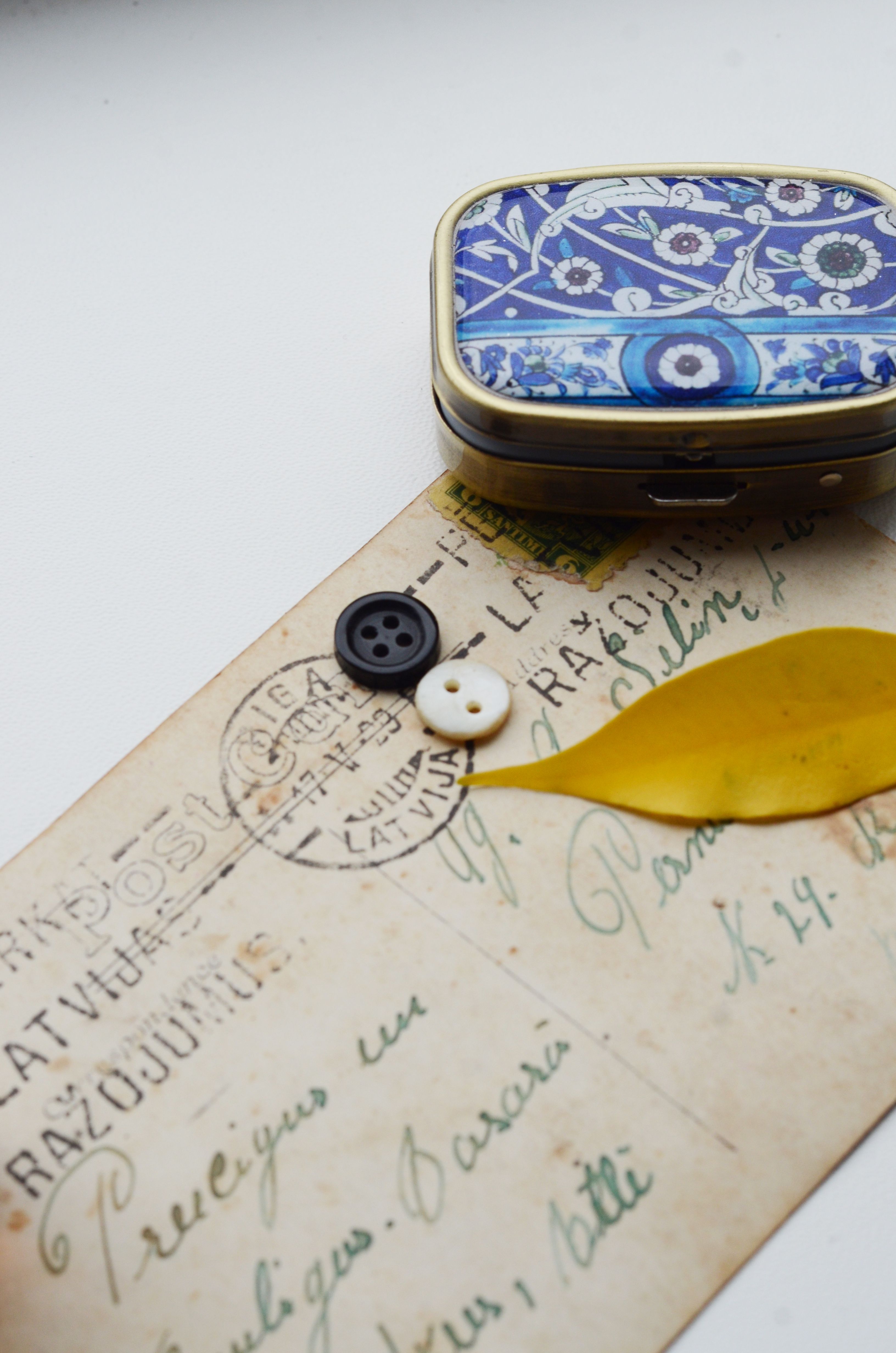 A close-up of a vintage postcard with decorative tin, buttons, and a leaf.