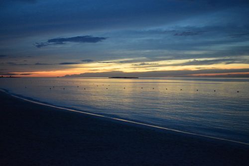 Free Serene beach view at twilight with calm waters and distant island, perfect for relaxation themes. Stock Photo