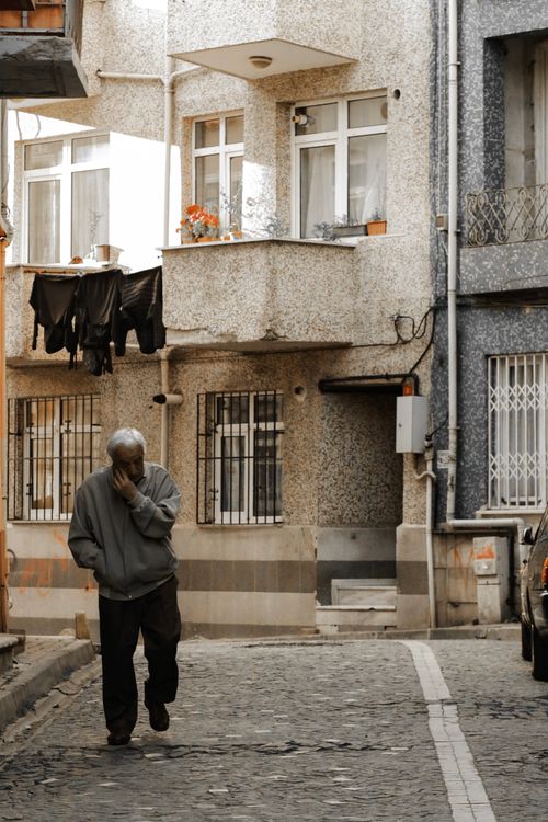 Free A senior man walks on a cobblestone street in Istanbul, wearing casual clothing, surrounded by residential buildings. Stock Photo