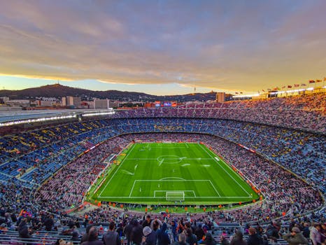 Aerial view of Camp Nou stadium filled with spectators during a football match at sunset in Barcelona, Spain.