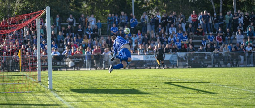 Intense soccer match with player heading ball towards goal, thrilling crowd in the background.