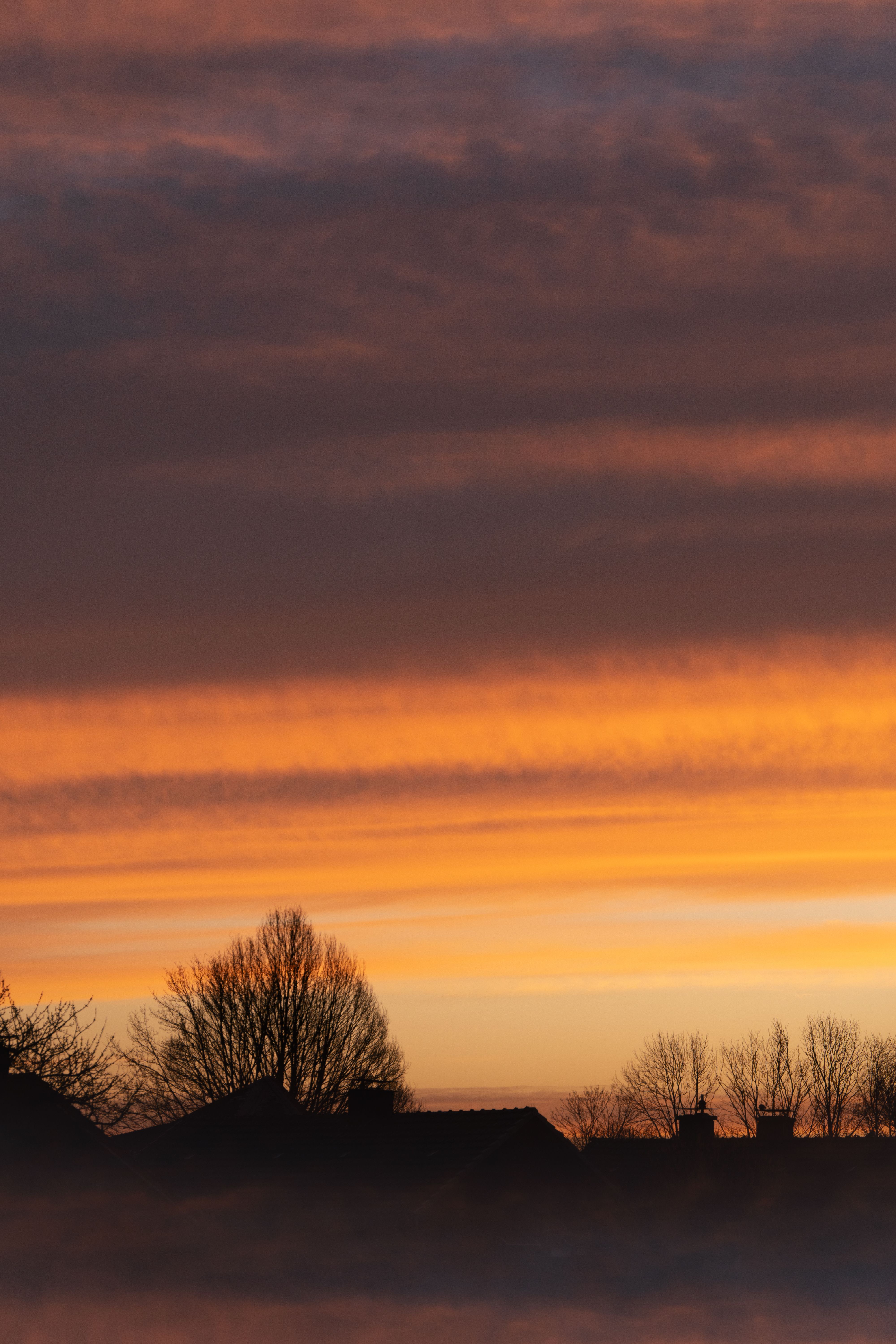 Silhouetted rooftops and trees under a vivid sunset sky in Gescher, Germany.