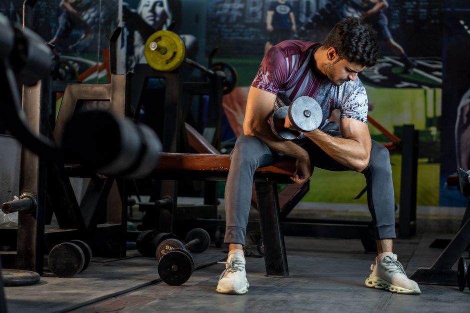 A muscular man working out in a gym, lifting a dumbbell for strength training.