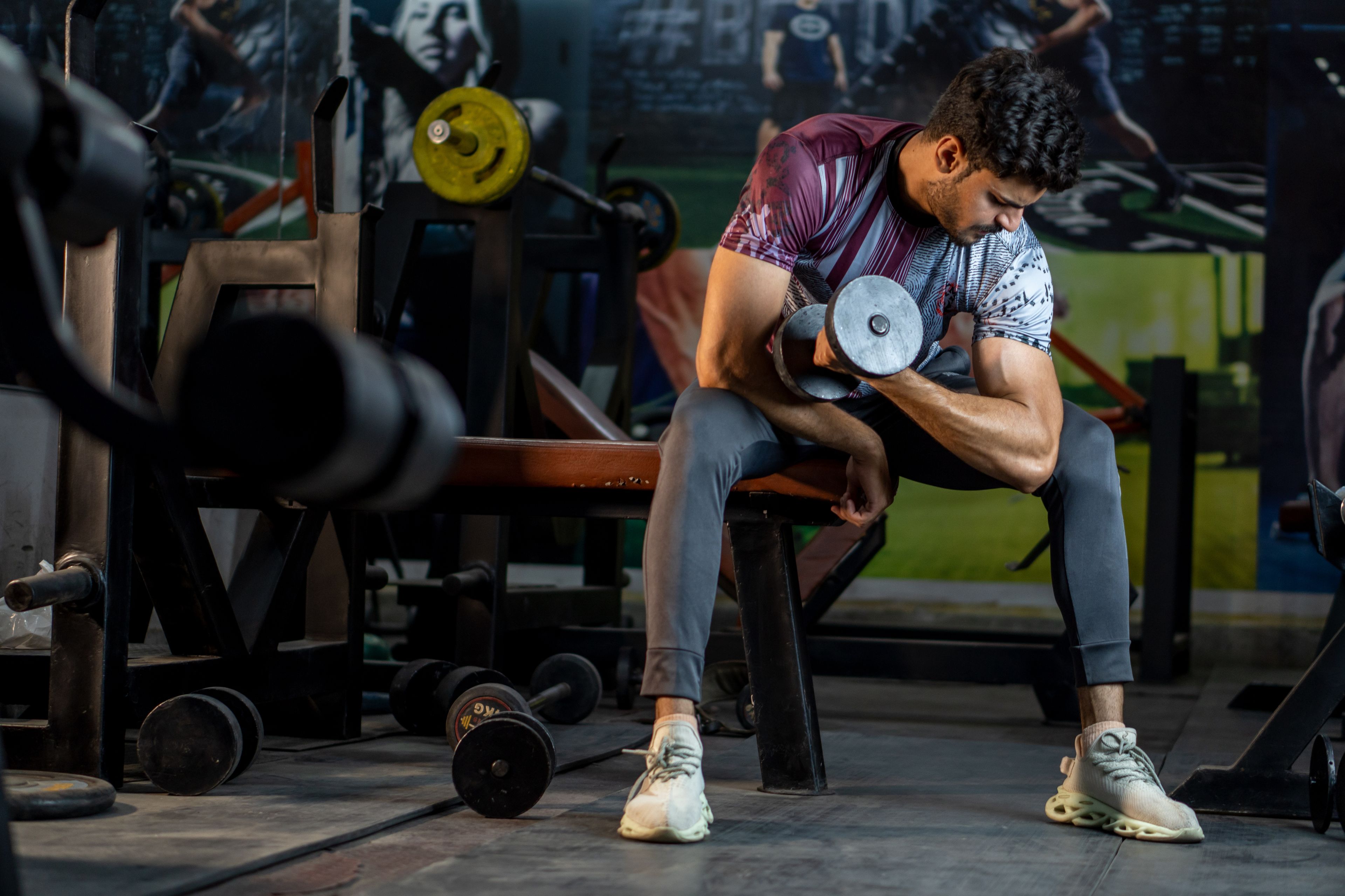 A muscular man working out in a gym, lifting a dumbbell for strength training.