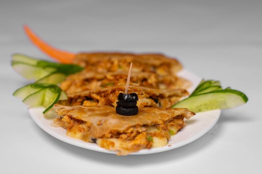Close-up of a tasty quesadilla garnished with cucumber and olive on a white plate.