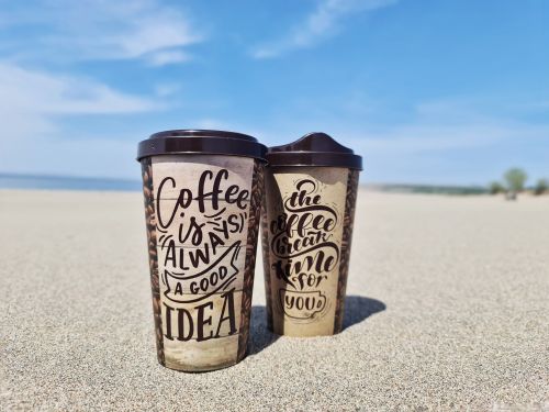 Free Stylish coffee cups on a sandy beach under a bright blue sky. Stock Photo