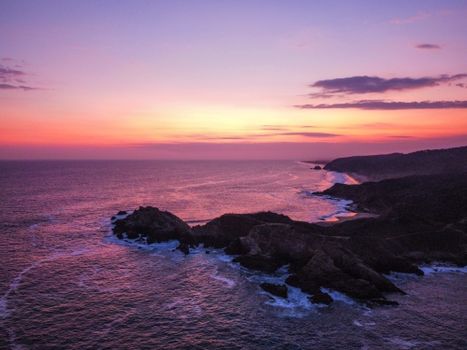 A breathtaking aerial view of a rocky ocean coastline illuminated by a vibrant sunset.