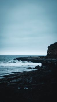 A moody view of a rocky coastline meeting the sea under an overcast sky, evoking a sense of solitude.