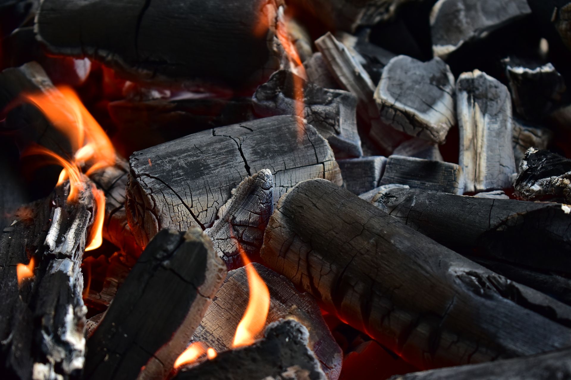 Detailed shot of glowing charcoal embers with vibrant flames against a dark background.