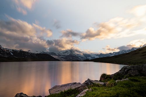 Calm Lake near Snow Capped Mountains under Cloudy Sky