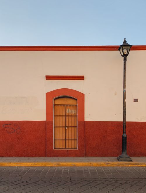 Free Vibrant red and white building facade with a vintage lamp post on a quiet street. Stock Photo