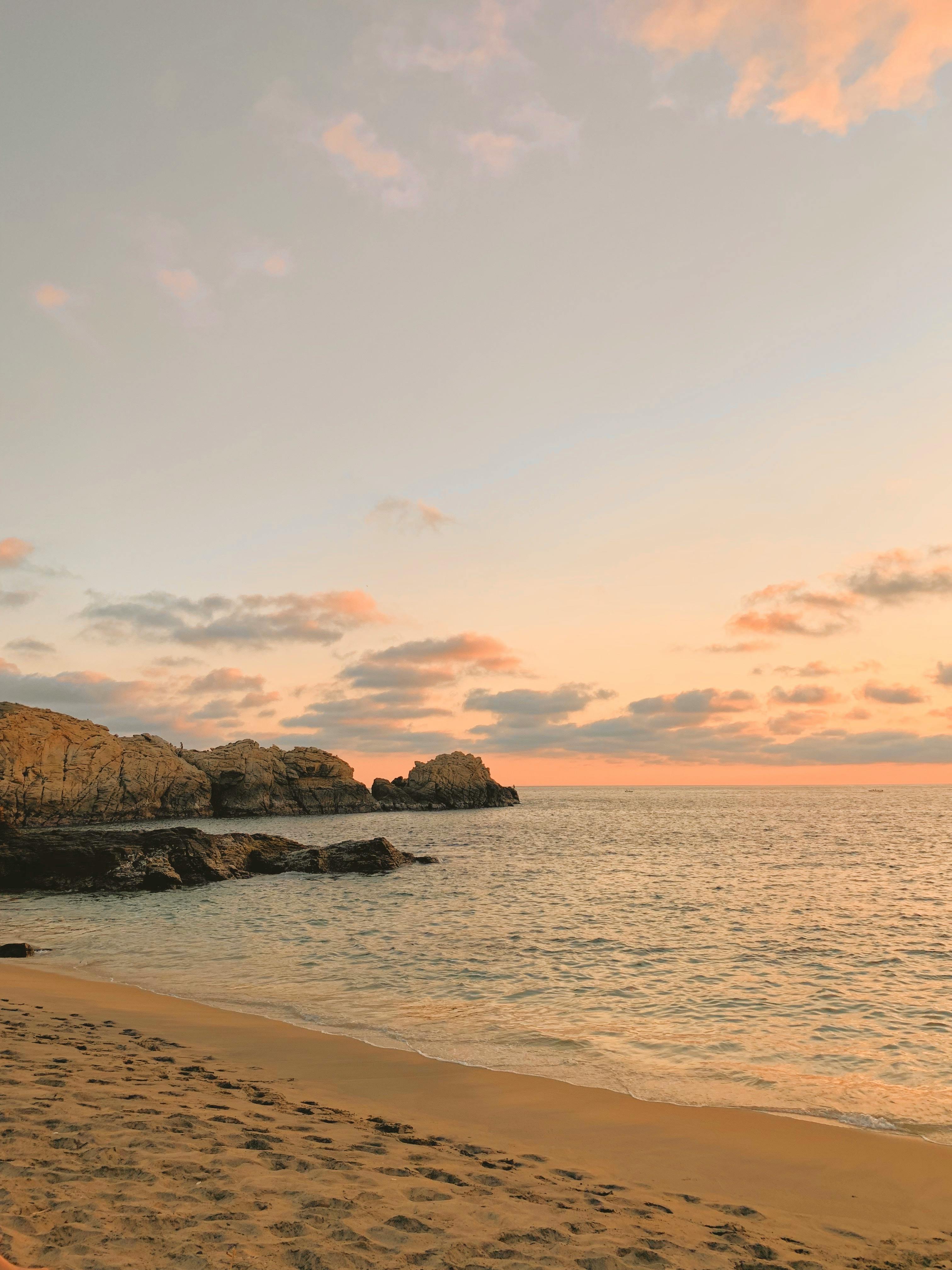 A peaceful sunset at the beach featuring golden skies and ocean waves crashing against rocky cliffs.