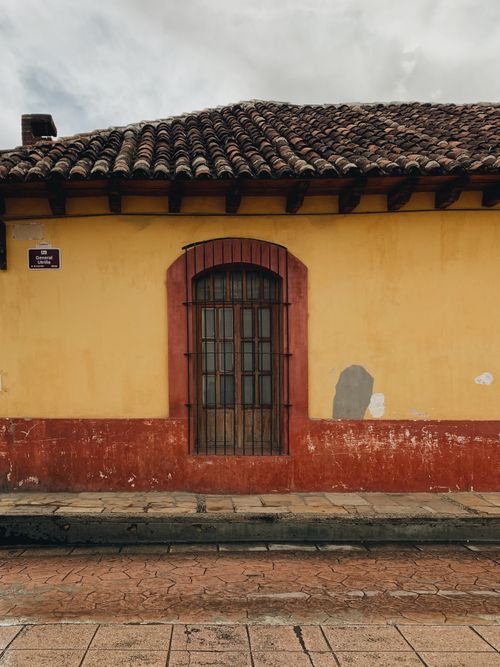 Free A vibrant yellow colonial facade with a wooden arched doorway on a cobblestone street. Stock Photo