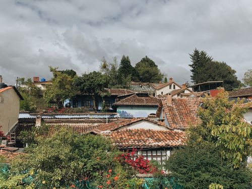 Free Explore charming village scenery with terracotta roofs and lush greenery under a moody sky. Stock Photo