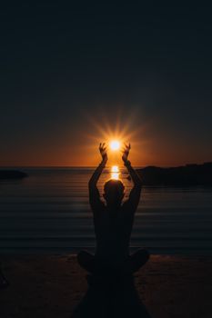 Person meditating at sunset on Puertecitos Beach, Mexico, with sun between raised hands.