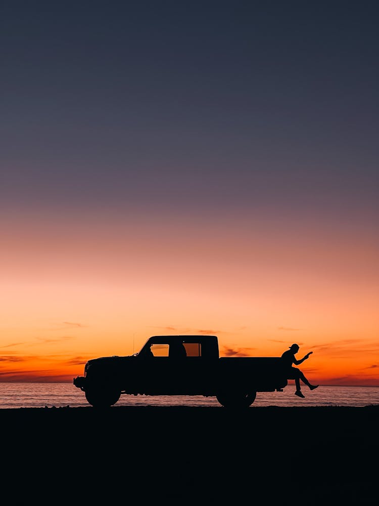 Person Sitting On Car Trunk On Shore