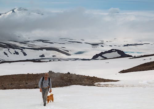 Free A Man Walking on Snow Covered Ground with His Dog Stock Photo