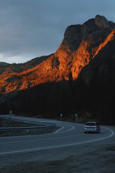 A car on a winding road with mountains illuminated by the setting sun.