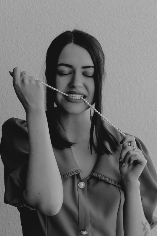 Free Black and white portrait of a woman playfully biting a pearl necklace with eyes closed. Stock Photo