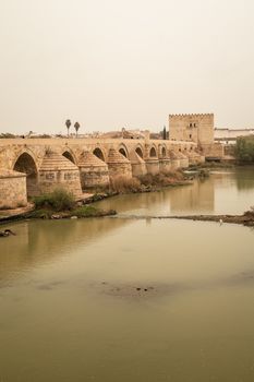 Historic Roman bridge spanning the Guadalquivir River in Córdoba, Spain, showcasing ancient architecture.