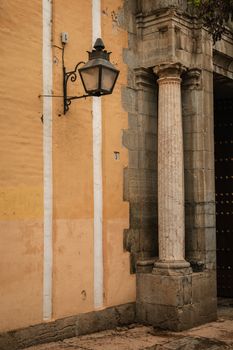 Classic stone column and vintage streetlamp on a yellow wall in Córdoba, Spain.