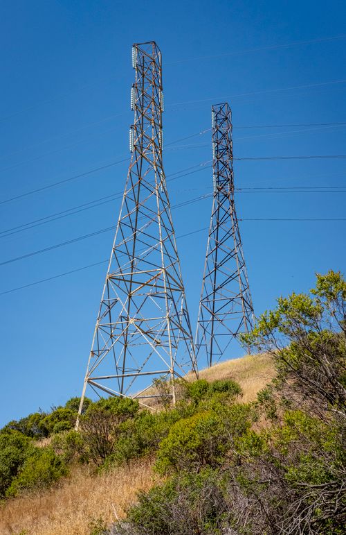 Free Two electric towers rise above a hill under a clear blue sky, capturing industrial progress. Stock Photo