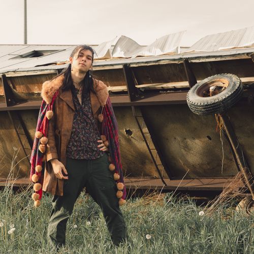Free Fashionable man posing confidently by a rustic overturned trailer in a grassy field. Stock Photo