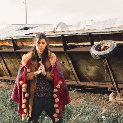 Free Man in a fashionable outfit stands confidently outdoors, showcasing boho style. Stock Photo