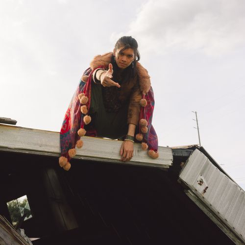 Free Fashion-forward man posing on a rooftop edge in a colorful cape against a cloudy sky. Stock Photo