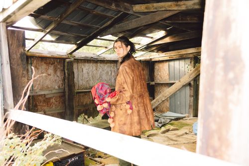 Free A young woman poses in a rustic interior, wearing a stylish jacket and holding a patterned fabric. Stock Photo