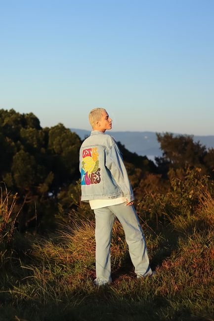 Man wearing trendy denim jacket outdoors in nature during sunset.