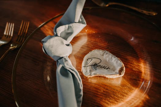 Stylish dinner table setting featuring a seashell place card and cloth napkin on wood.