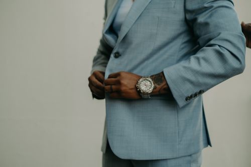 Free A stylish man in a light blue suit adjusts his button showcasing elegance and sophistication. Stock Photo
