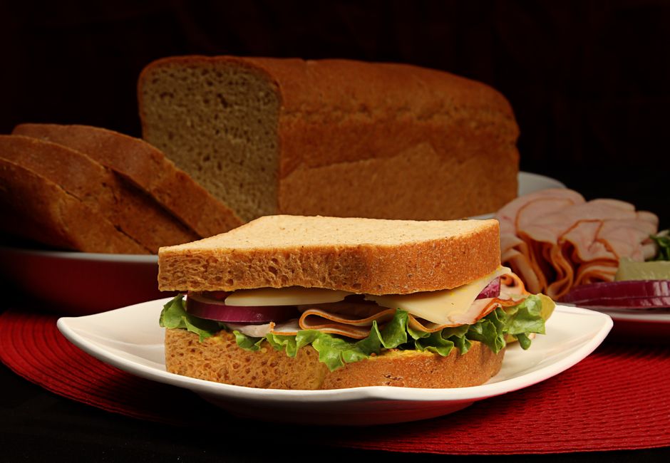 A sliced loaf of gluten free bread on a wooden board, showing an even, tight crumb and a golden brown crust with a few slices fanned out in front.