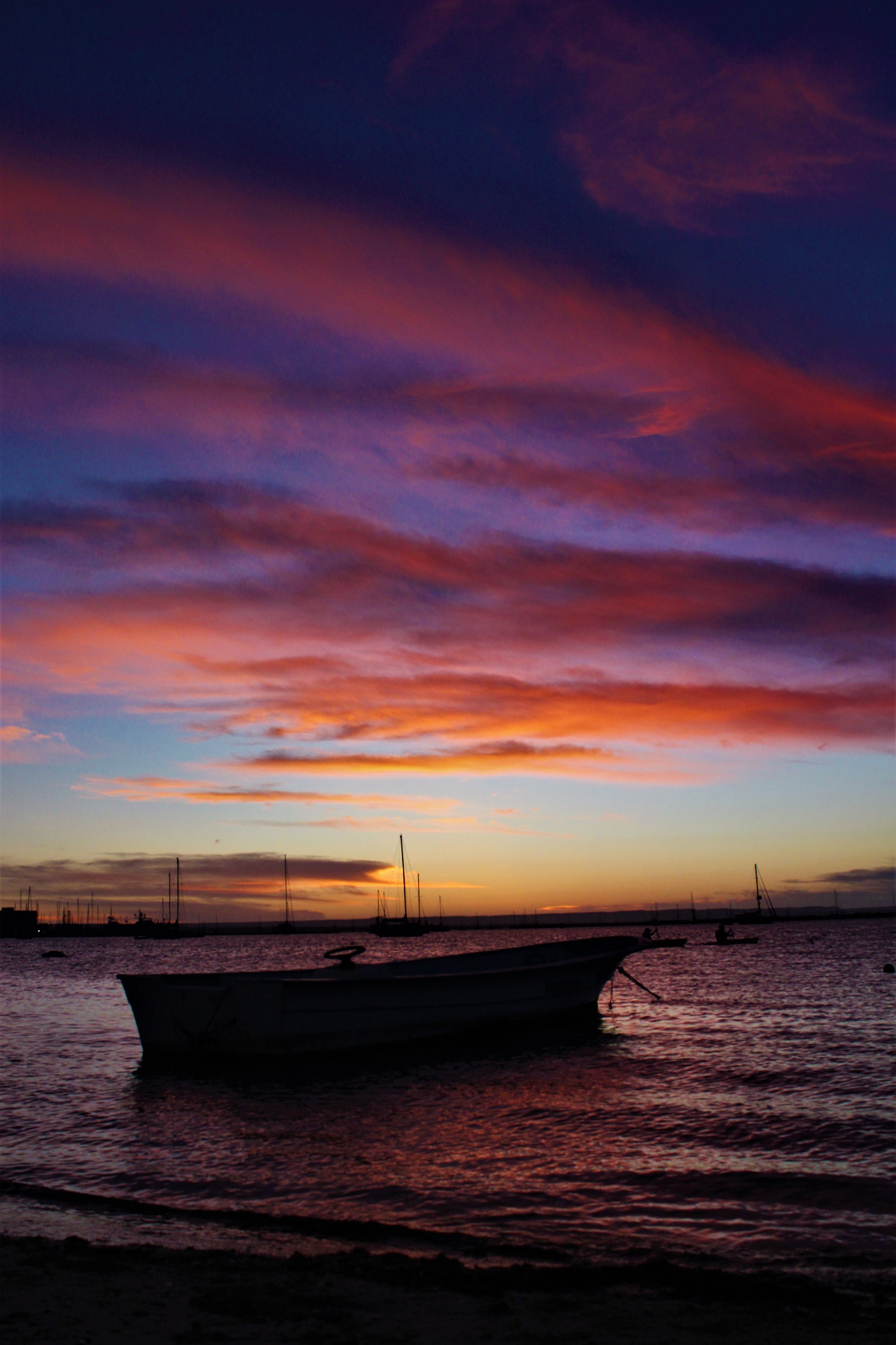 A serene sunset view over a harbor with boats silhouetted against a dramatic sky.