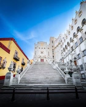 Grand staircase leading to University of Guanajuato under clear blue sky, showcasing neoclassical architecture.