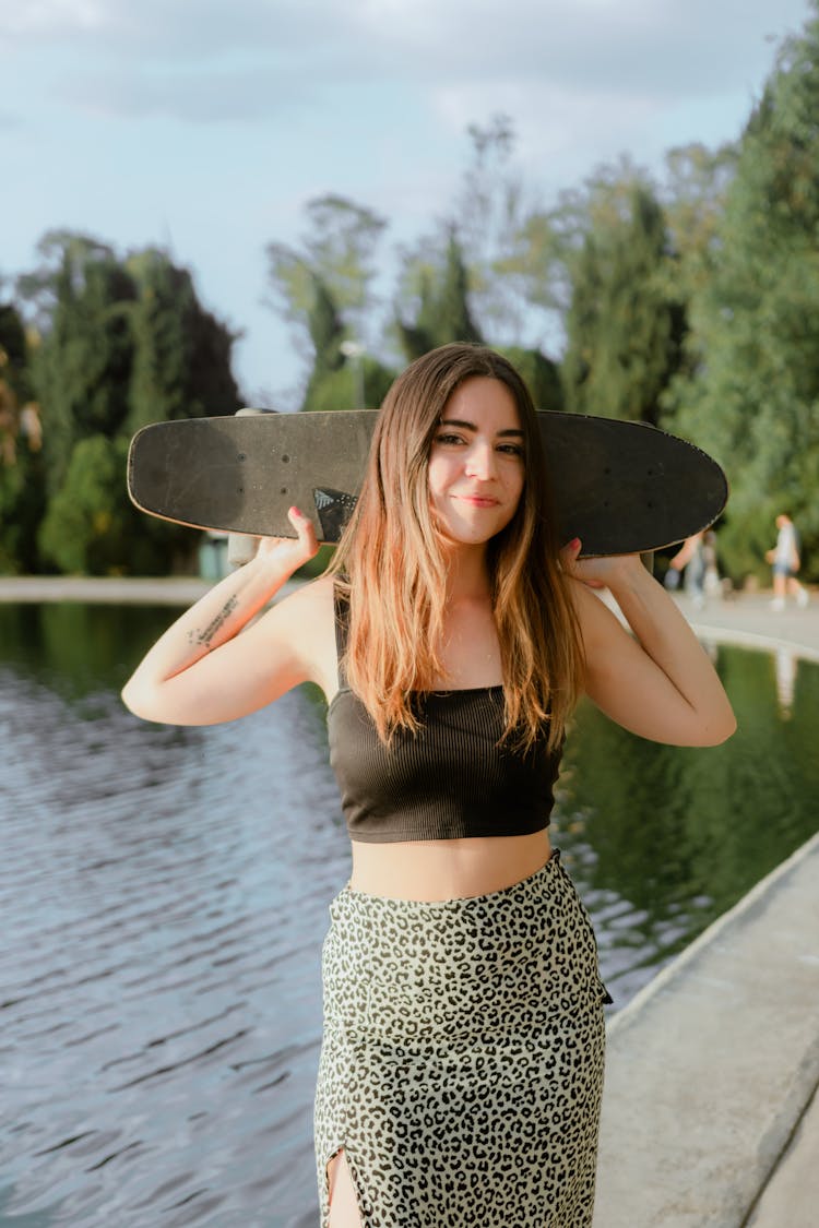 Smiling Girl Standing By A Pond Holding A Skateboard